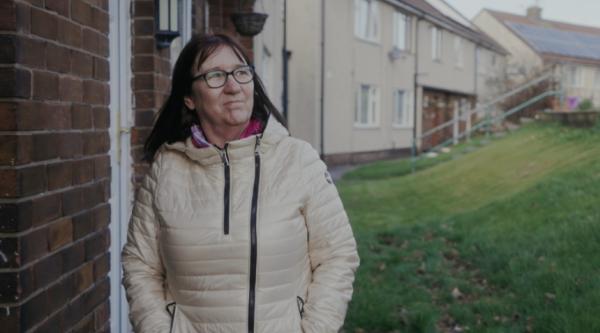 Gina walking through the neighbourhood wearing a coat with her hands in her pockets and smiling