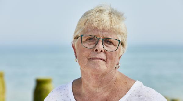 A woman with short blonde hair and glasses with the sea behind her